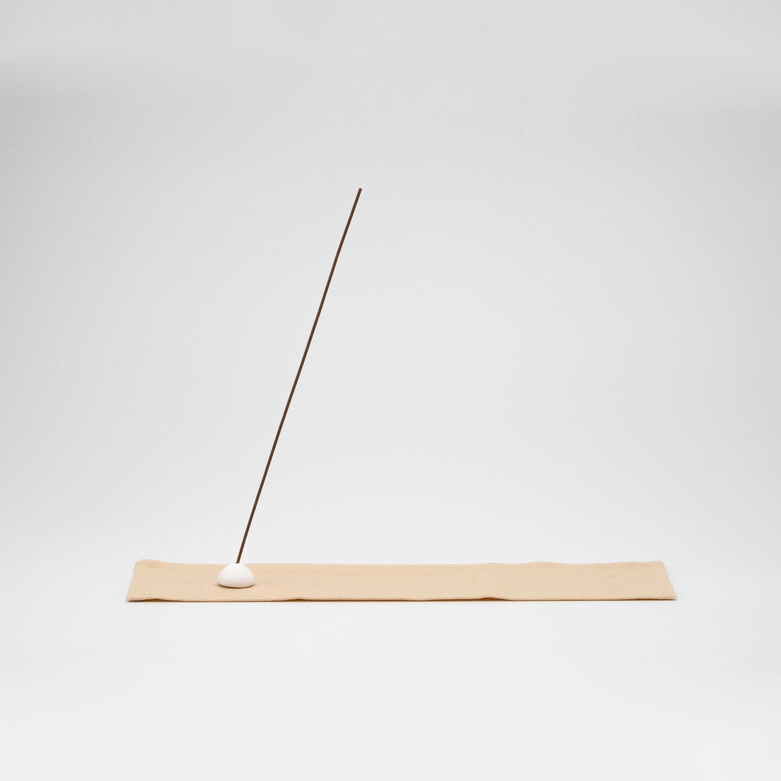 Minimal incense stick holder featuring a white ceramic bead on a soft beige cotton mat, with ash-catching surface and natural tones.