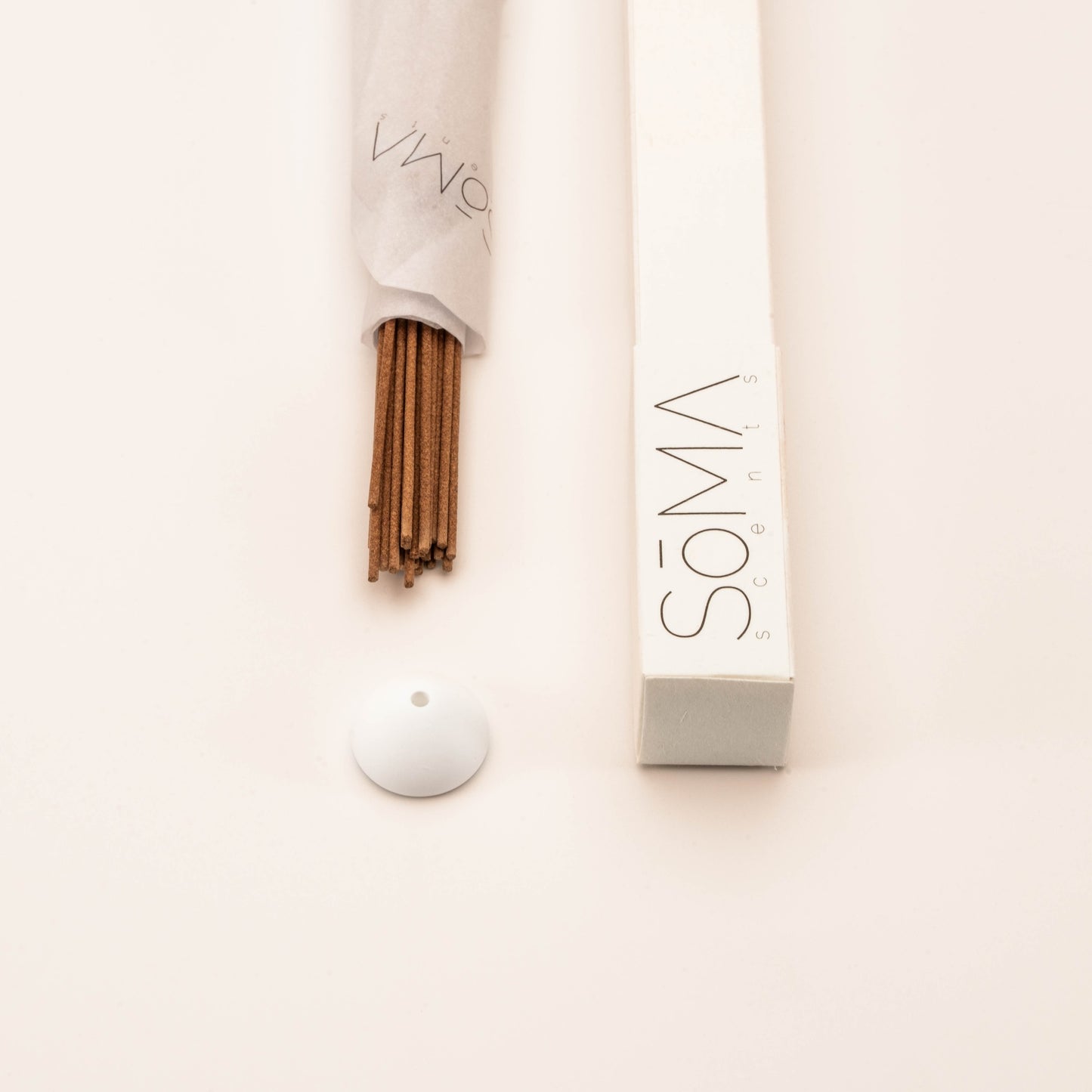 Close-up of SomaScents traditional incense sticks partially wrapped in branded paper, with white minimalist box and holder.