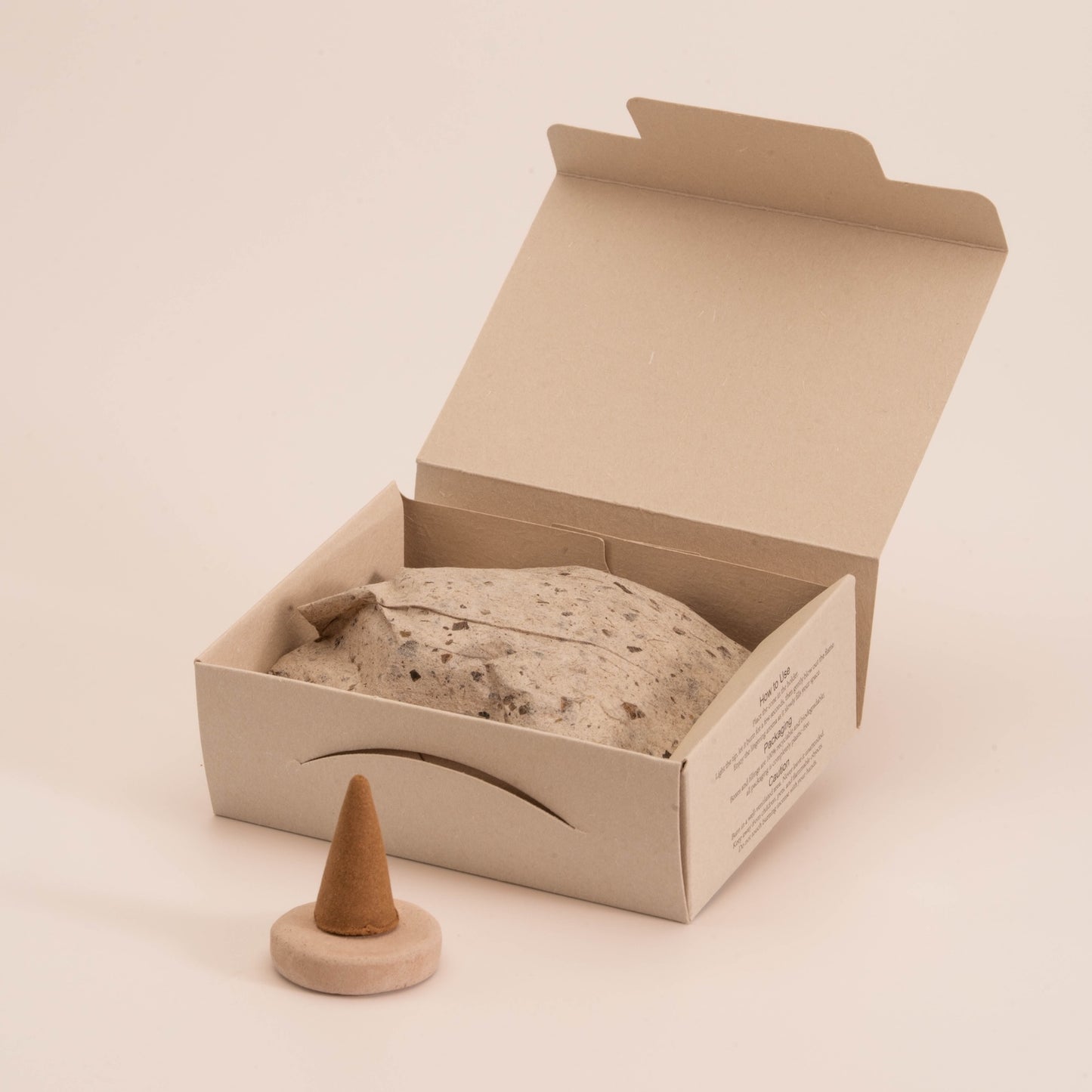 Close-up of SomaScents incense cone packaging with eco-friendly brown box, seeded wrapping paper, and a single incense cone placed on a handmade holder.