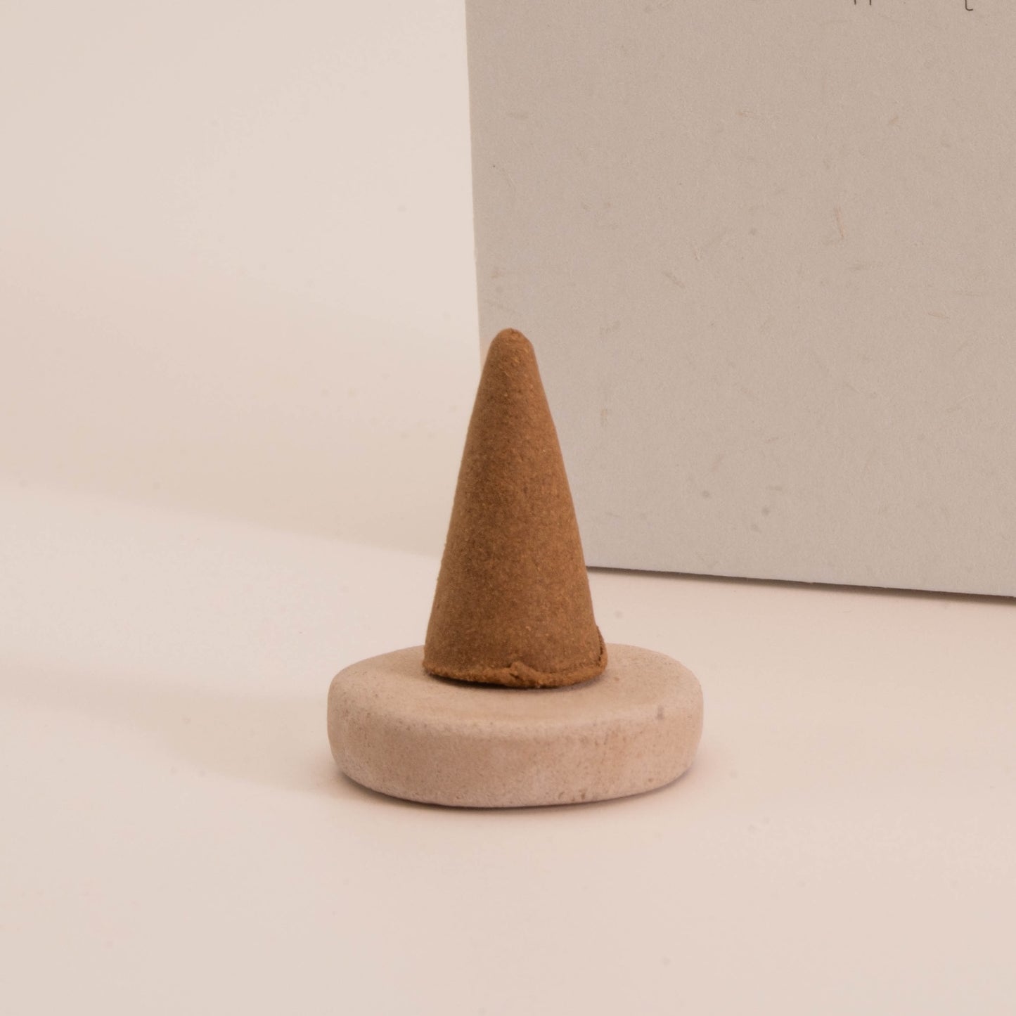 Close-up of a SomaScents brown incense cone placed on a round ceramic holder