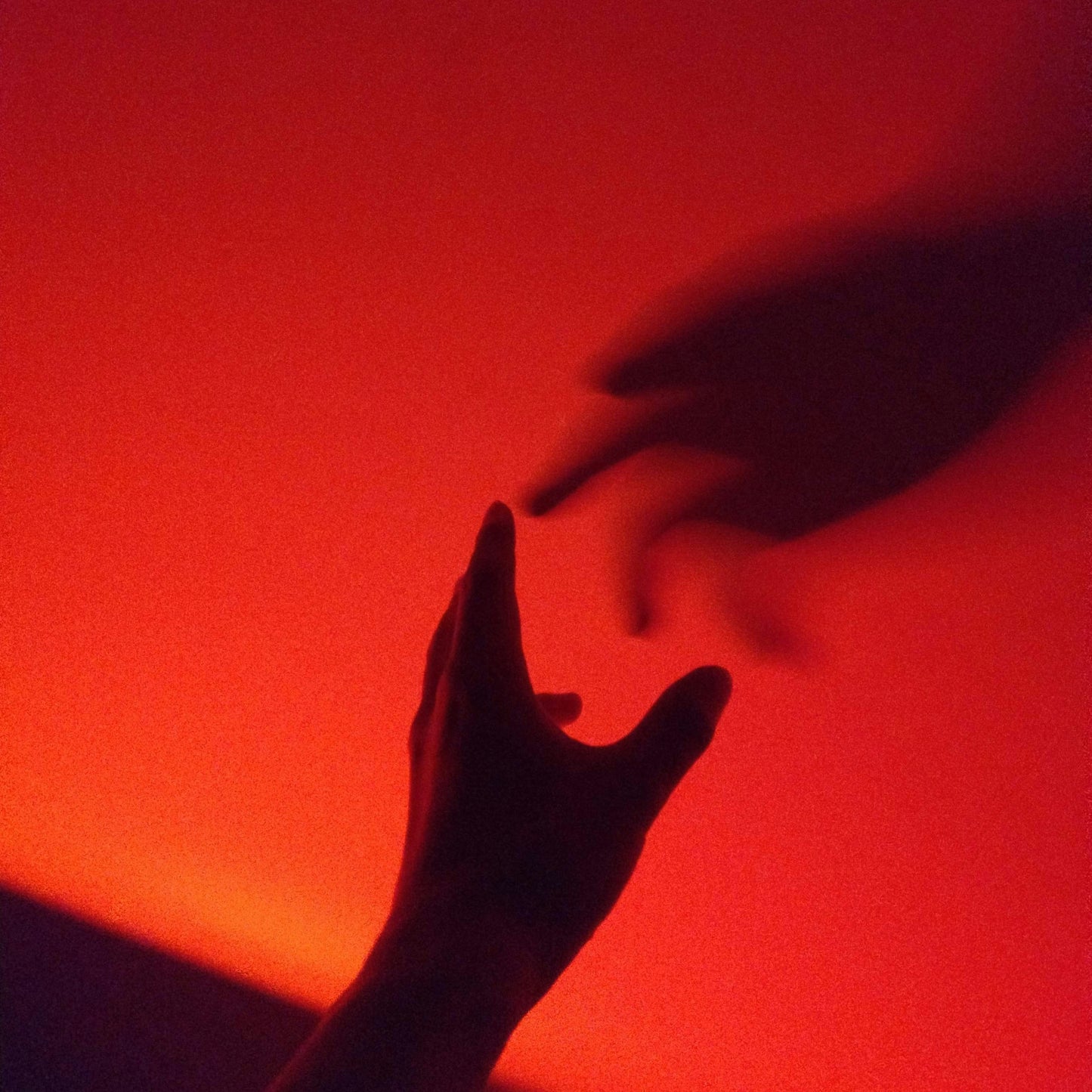 Two silhouetted hands reaching toward each other in red lighting.
