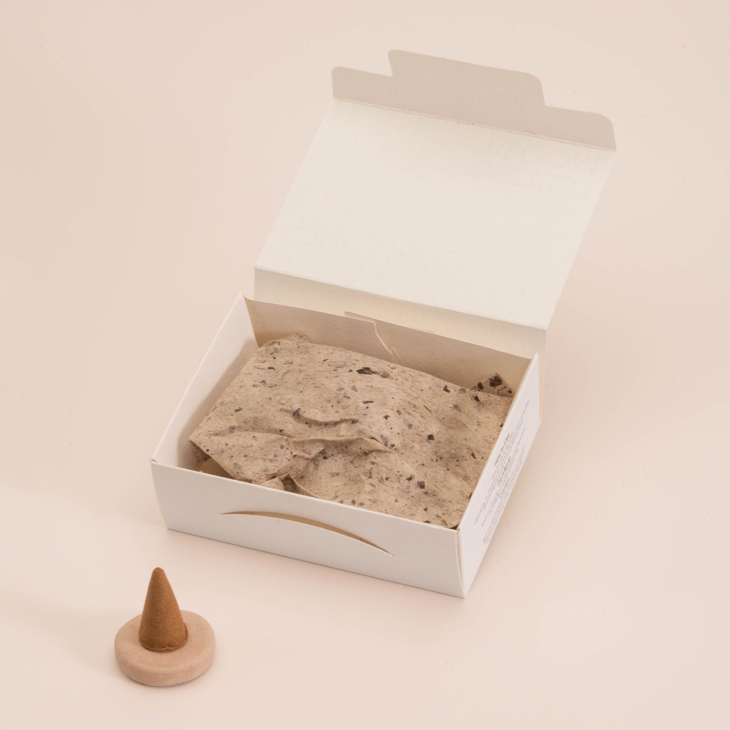 Close-up of SomaScents incense cone packaging with eco-friendly white box, seeded wrapping paper, and a single incense cone placed on a handmade holder.