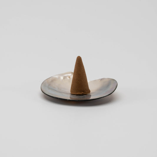 Iridescent mother-of-pearl shell incense cone holder with natural curves and soft shimmer, placed on a clean white surface.