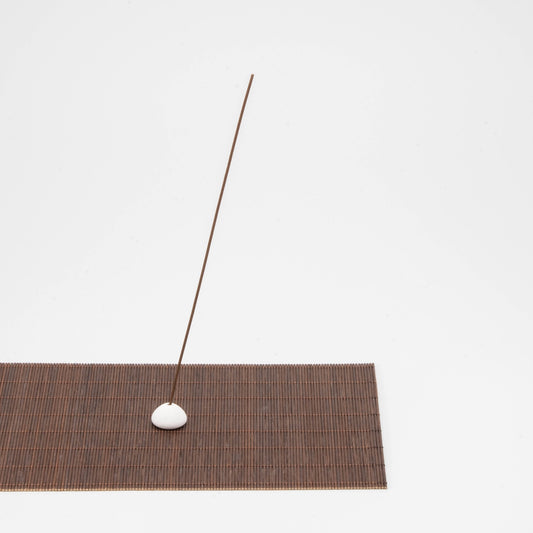 Incense stick holder with a white ceramic bead placed on a rectangular bamboo mat