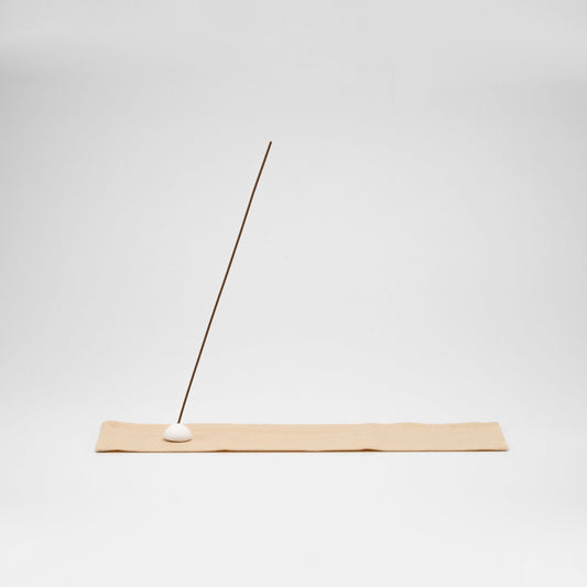 Minimal incense stick holder featuring a white ceramic bead on a soft beige cotton mat, with ash-catching surface and natural tones.