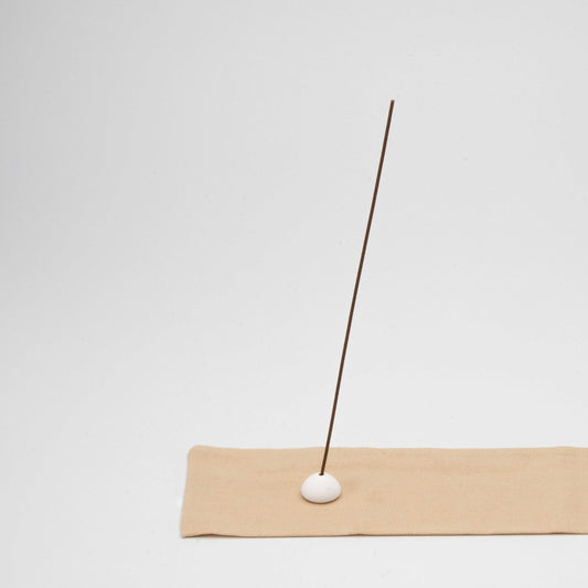 Close-up of textured cotton fabric with a stitched edge, showing detail of the beige incense mat and ceramic holder.