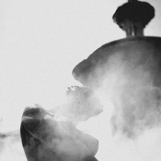Stone statue enveloped in smoke under bright sunlight in grayscale tones.