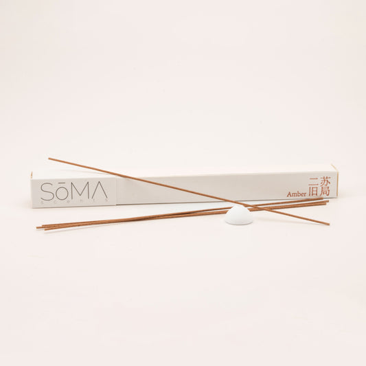 SomaScents Amber incense sticks with beige packaging, red Chinese and English text, and a white ceramic holder on a soft neutral background.