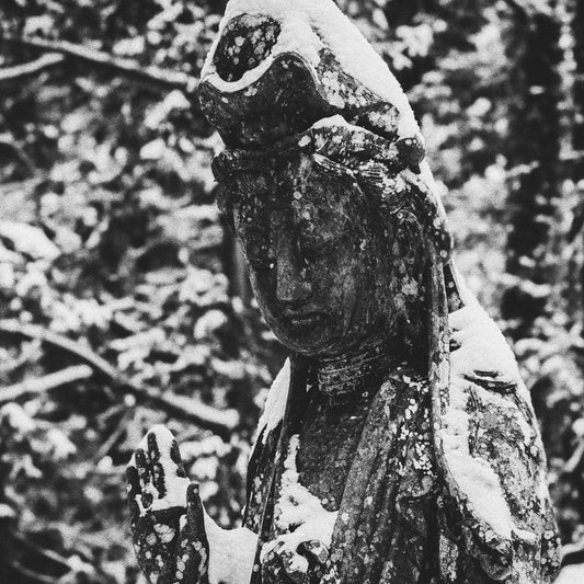 Snow-covered ancient statue of a serene figure in a forested scene.