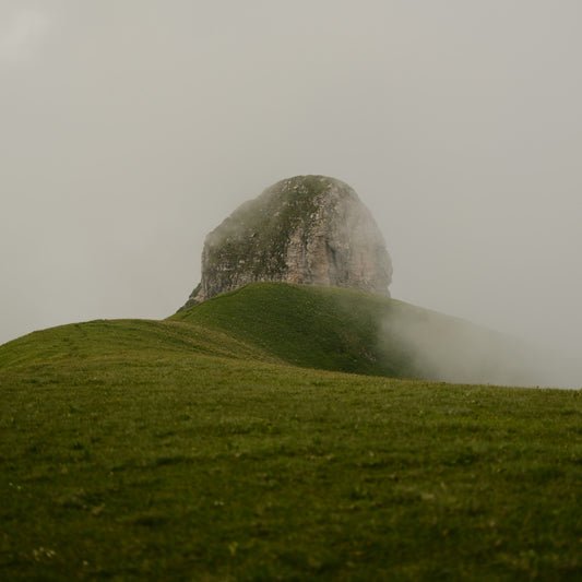 Fog rolls over a grassy hill with a rocky summit