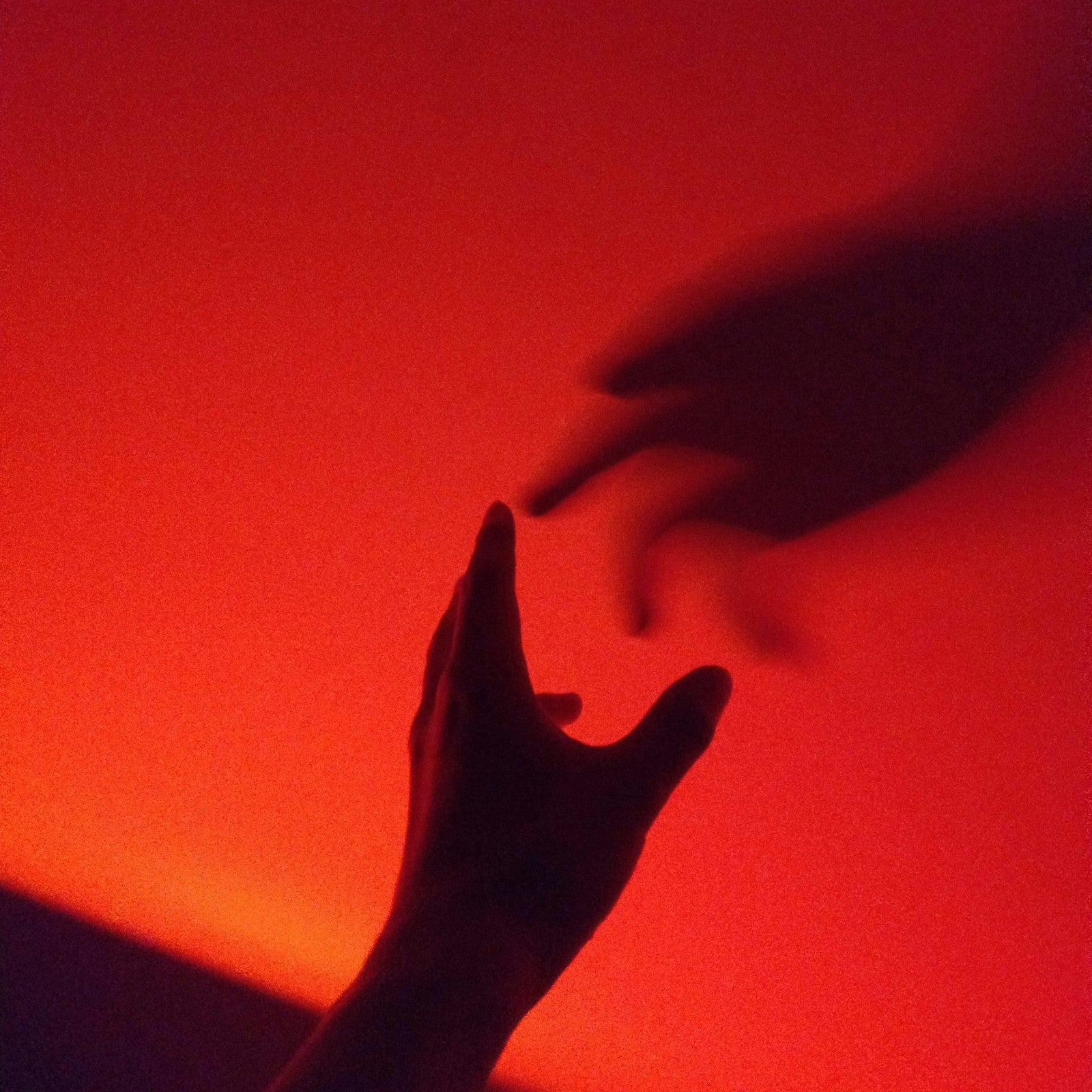 Two silhouetted hands reaching toward each other in red lighting.