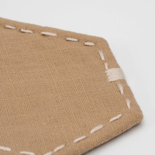 Close-up of tan linen fabric with visible white stitching, showing texture and detail of the handcrafted incense mat.