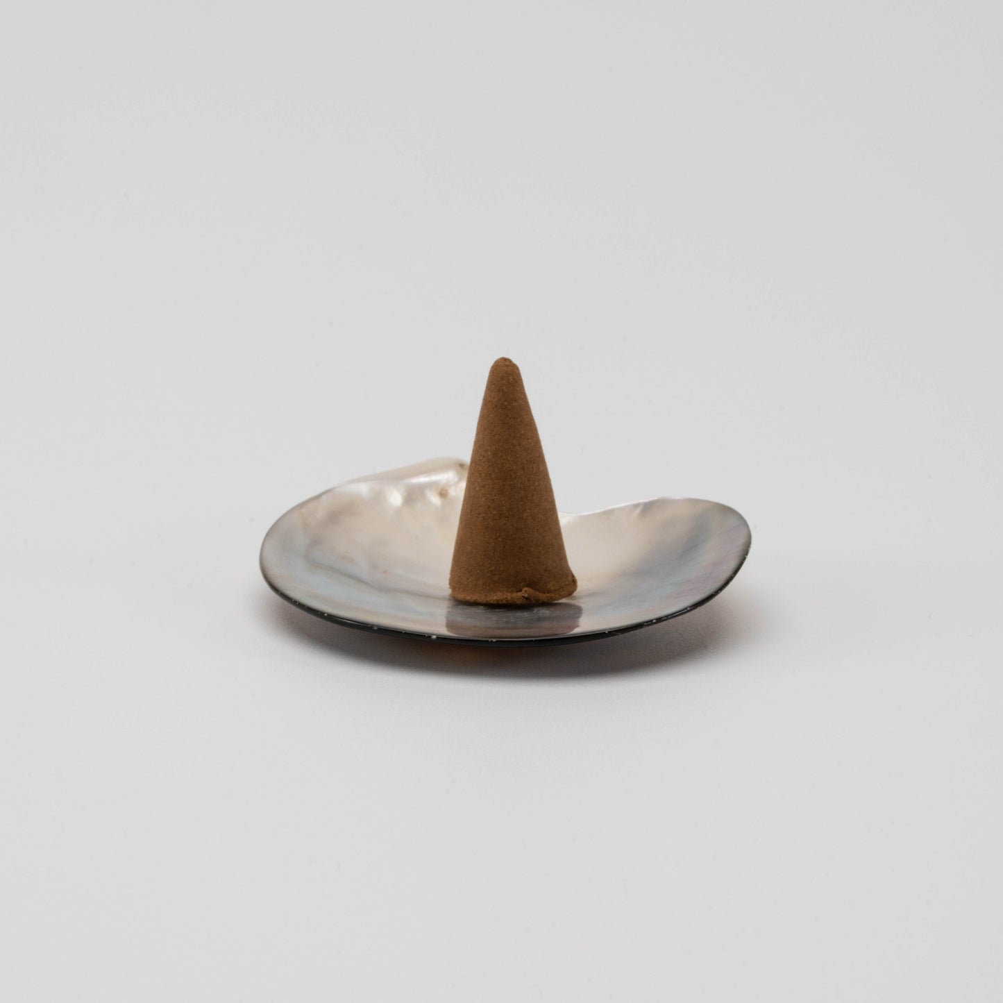 Iridescent mother-of-pearl shell incense cone holder with natural curves and soft shimmer, placed on a clean white surface.