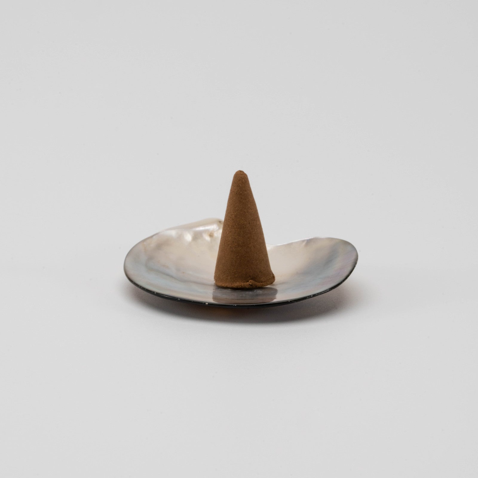 Iridescent mother-of-pearl shell incense cone holder with natural curves and soft shimmer, placed on a clean white surface.