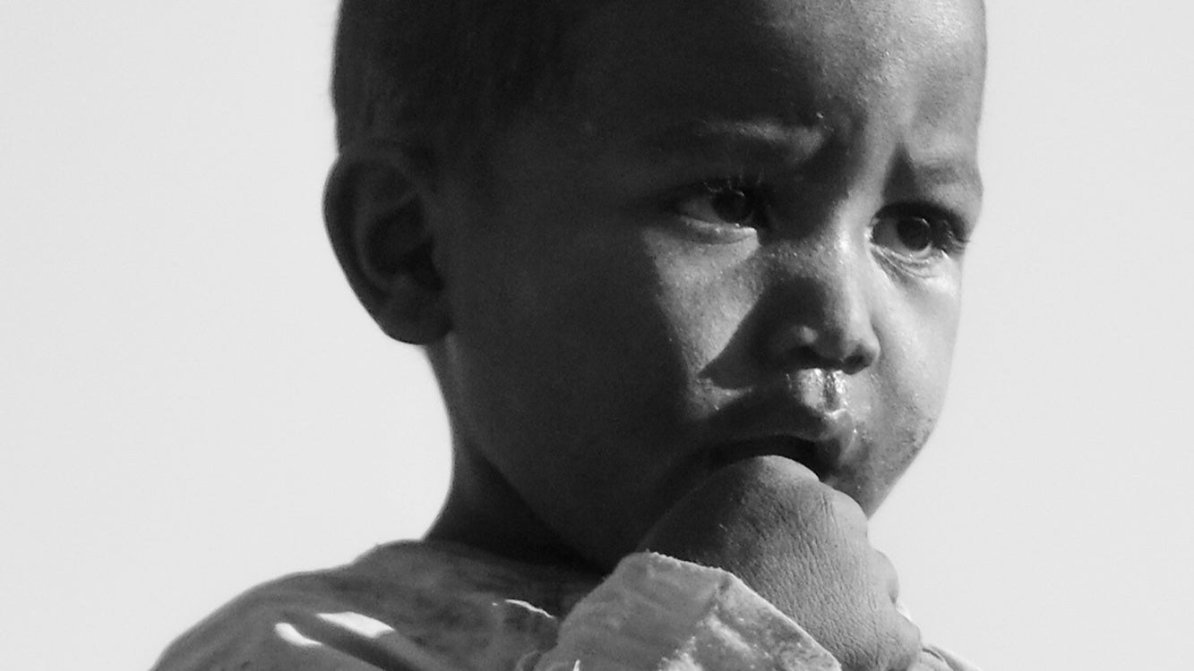 Close-up of child in worn clothing staring with thoughtful eyes